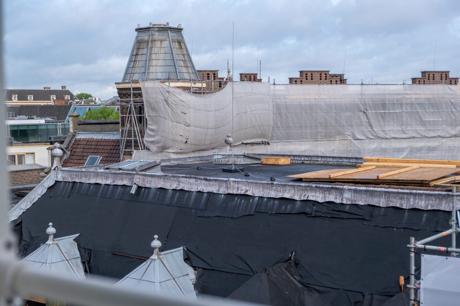 Roof construction, insulation works and tiling. Metal scaffolding, timber and waterproofing membrane at building rooftop. Amsterdam, Netherlands